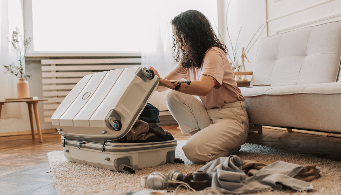 A woman packing a suitcase on the floor next to a bed, preparing for travel.