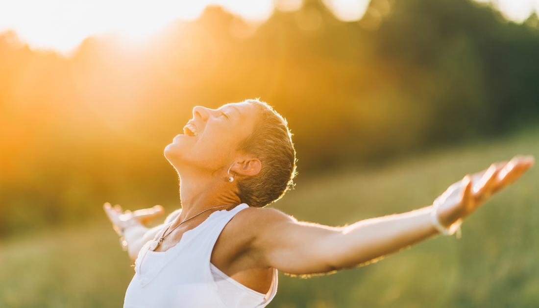 woman smiling up at the sun in a meadow with her arms out wide